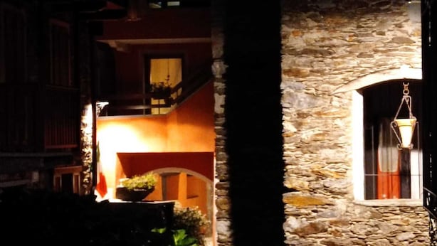 A stone building with a hanging lantern, a balcony, and a window with curtains. - LA GHIANDA APPARTAMENTO CON TERRAZZO ANIMALI AMMESSI (Cossogno)