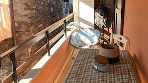 A cozy balcony with a checkered tablecloth, a stone wall, a wooden ceiling, and a view of a building in the background. - LA GHIANDA APPARTAMENTO CON TERRAZZO ANIMALI AMMESSI (Cossogno)