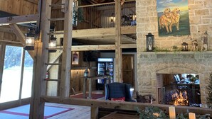 Un intérieur spacieux avec un haut plafond en bois, un lustre, une cheminée et un tableau représentant des chiens.