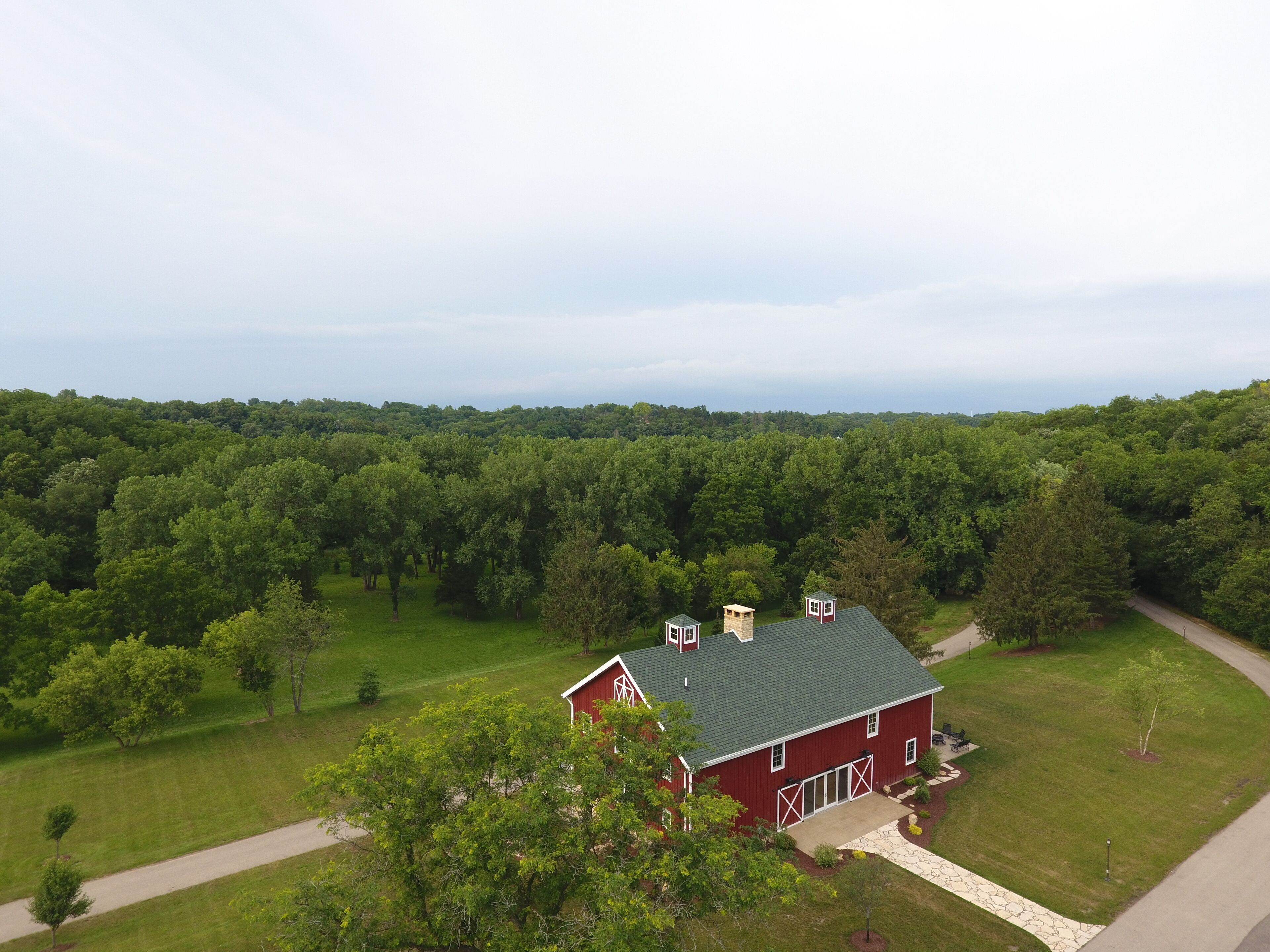A red barn with a green roof, surrounded by lush green trees and a well-maintained lawn.