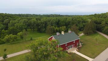 A red barn with a green roof, surrounded by lush green trees and a well-maintained lawn.