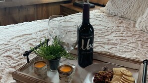 Une chambre confortable avec une tête de lit en bois, une lampe de chevet, une statuette de cheval décorative, une bouteille de vin, des verres, un plateau avec des amuse-gueules et une petite plante.
