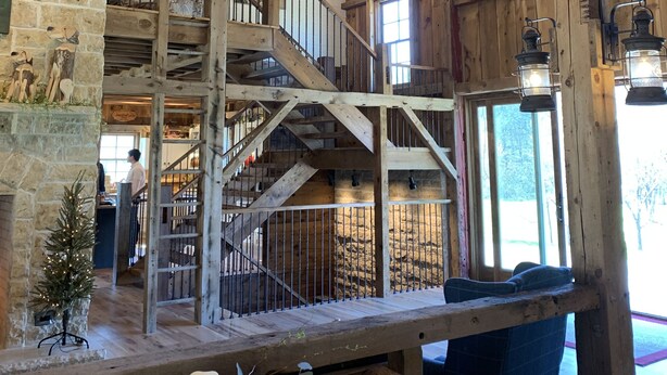 Un intérieur rustique avec des poutres apparentes, un escalier et un lustre.