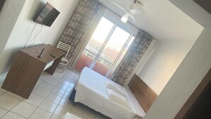 Habitación de hotel con cama, escritorio, silla, televisor montado en la pared y ventana con cortinas.