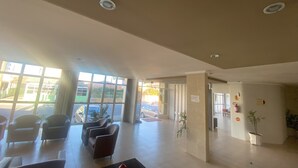 Un vestíbulo amplio con grandes ventanales, zona de estar y mostrador de recepción.