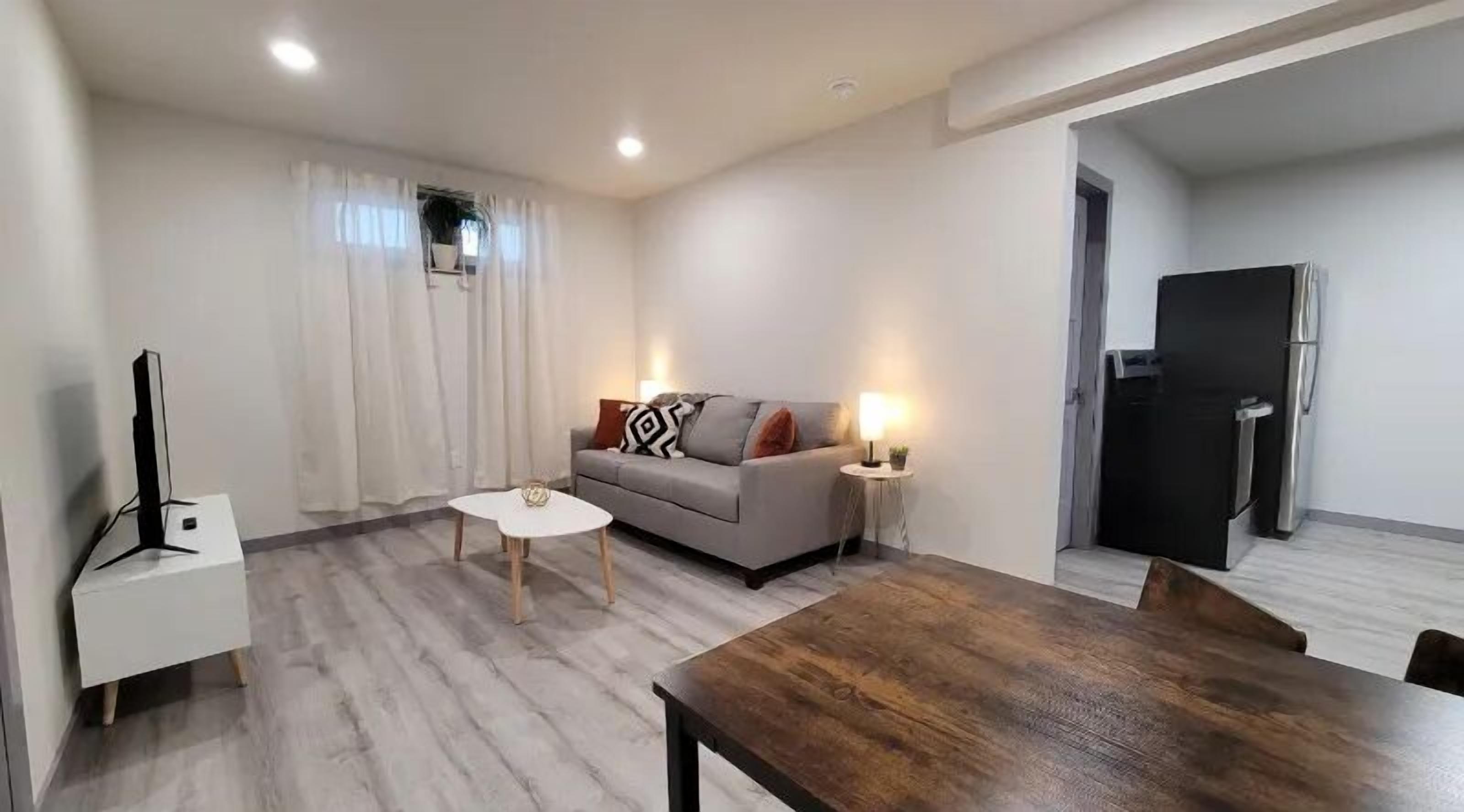 A modern living room with a grey sofa, a wooden dining table, and a TV stand.