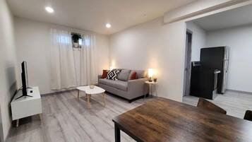 A modern living room with a grey sofa, a wooden dining table, and a TV stand.