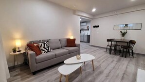 Un salon moderne avec un canapé gris, une table basse blanche et un coin repas comprenant une table et des chaises en bois.