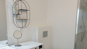 Une salle de bain moderne équipée d’un lave-linge, de toilettes et d’une douche à parois en verre.