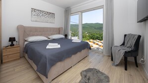 Une chambre à coucher comprenant un lit, une table de chevet, une chaise et donnant sur l’extérieur.