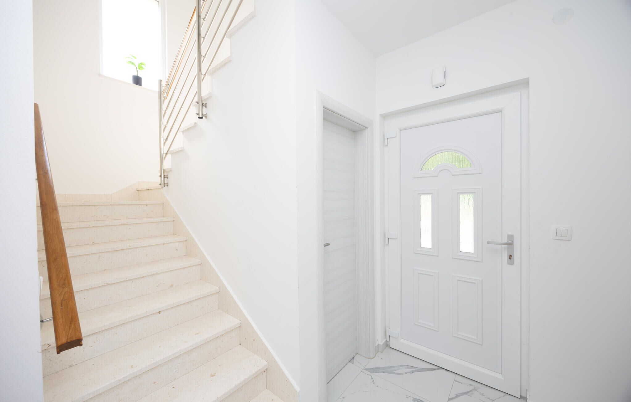 A staircase leading to a white door with a small window, a light switch, and a smoke detector on the wall.