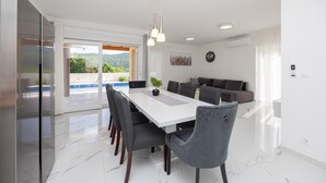Un espace de salle à manger moderne avec une table blanche, des chaises à revêtement gris et des luminaires suspendus.