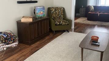 A living room with a flat-screen TV mounted on the wall, a wooden cabinet, a patterned armchair, a green sofa, and a coffee table.