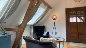 A cozy room with a sloped ceiling, a wooden door, a chair, a small table, and a floor lamp.