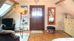 A cozy room with a wooden ceiling, a round table, a sofa, a mirror, and a wardrobe.