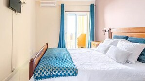 A hotel room with a bed, a bedside table, a TV, and an air conditioning unit. - White House (Altura)