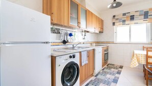 A compact kitchen with wooden cabinets, a washing machine, a sink, and a window with a view. - White House (Altura)