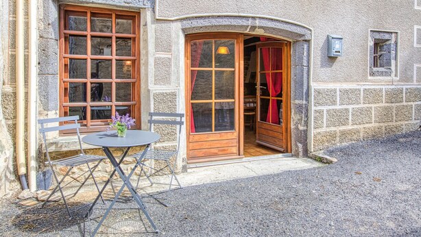 A stone building with a wooden door and windows, a gravel driveway, and a small table with chairs. - Gorgeous apartment in Saint-Chely-d'Aubrac (Saint-Chely-d'Aubrac)