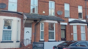 A two-story brick house with a white front door, a satellite dish, and a car parked in the driveway. - Woodstock Townhouse Belfast (Belfast)