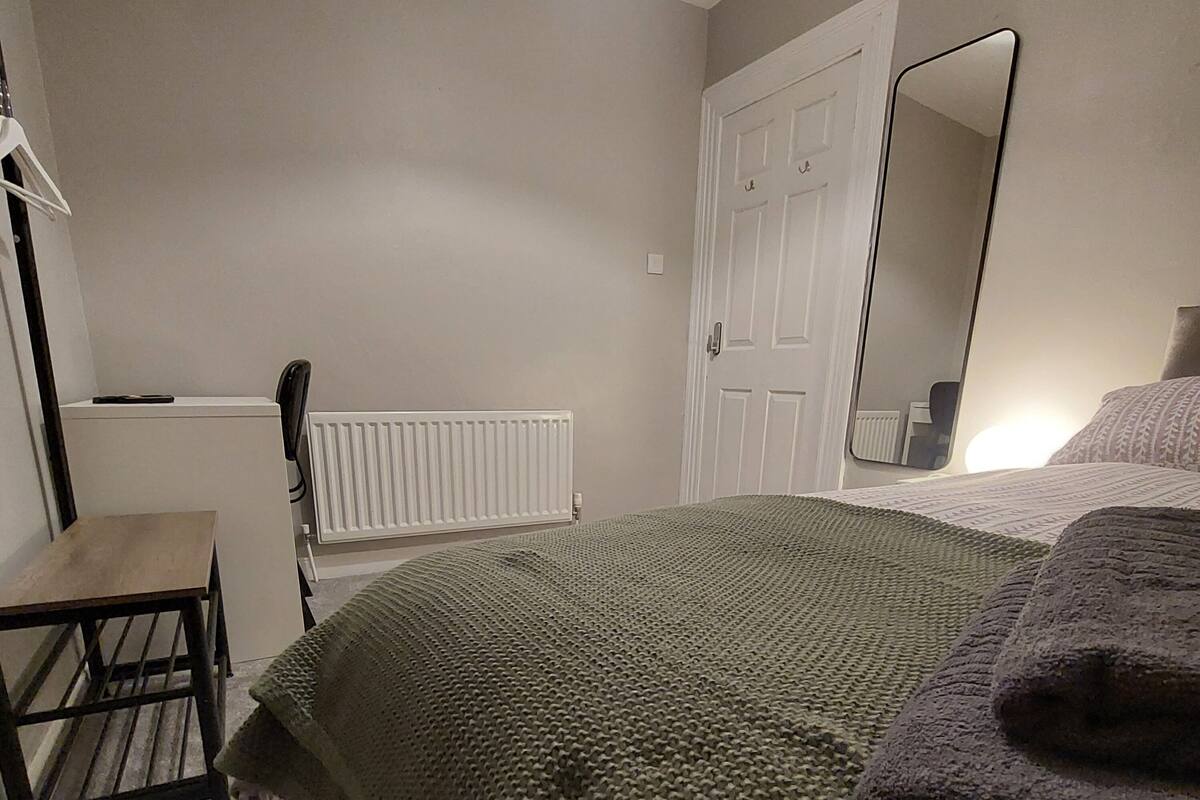 Un dormitorio con una cama, una silla, un radiador, una puerta y un espejo.