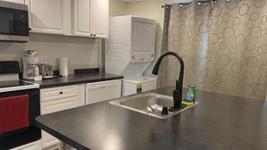 Una cocina compacta con gabinetes blancos, encimera negra, pileta de acero inoxidable y una toalla roja.