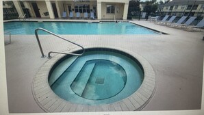 A swimming pool with a hot tub, lounge chairs, and a covered area with tables.