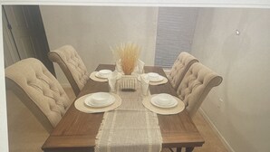 A dining area with a wooden table, six upholstered chairs, and a vase with dried plants.
