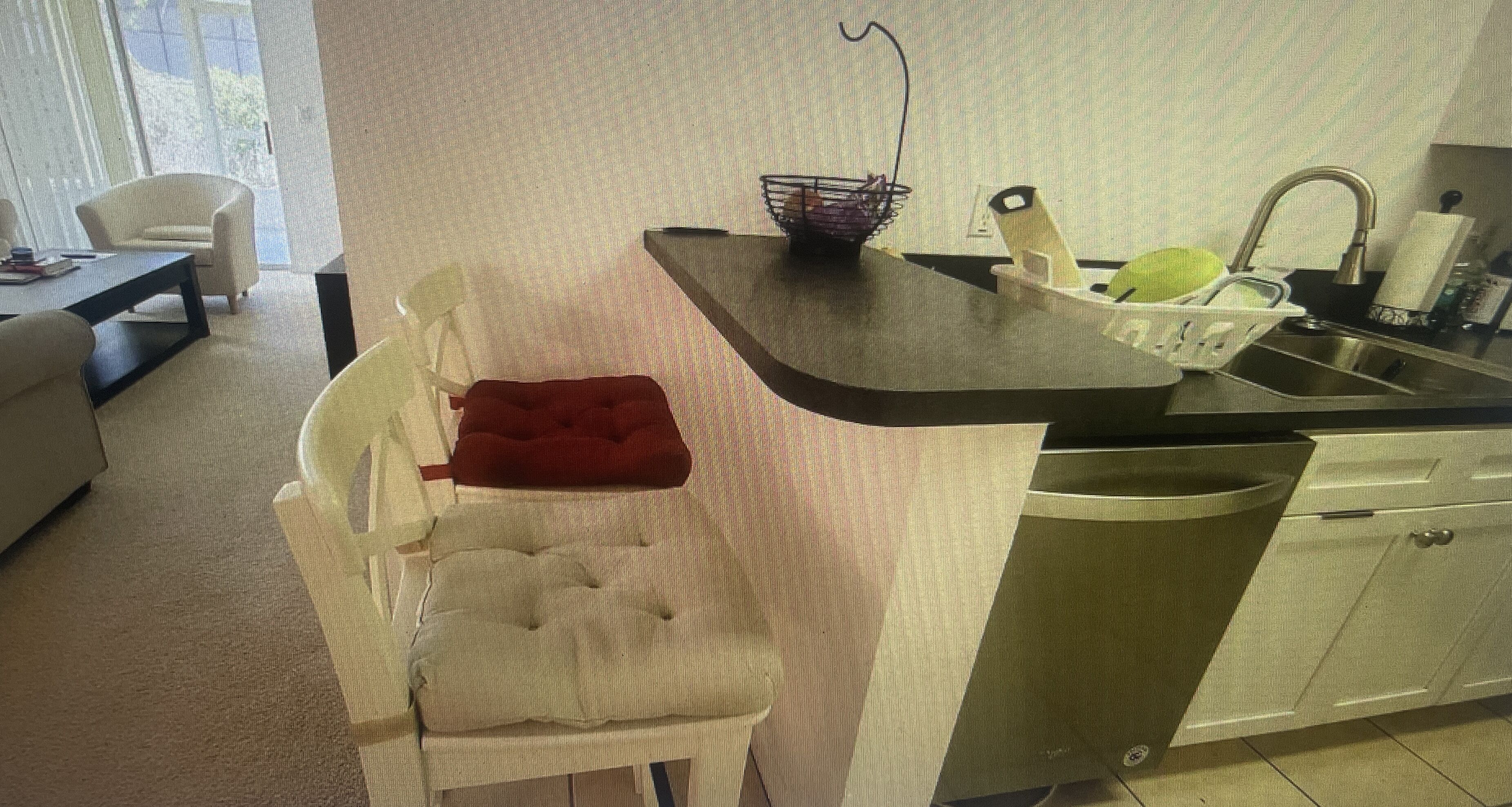 Uma cozinha compacta com máquina de lavar louça embutida, uma pia pequena com torneira e uma toalha vermelha em uma cadeira.