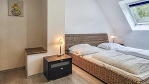 Una camera da letto con soffitto spiovente, un letto in vimini, due comodini con lampade e una piccola opera d'arte appesa al muro.