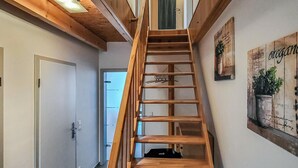 Una scala interna in legno conduce al secondo piano, con una porta e un'opera d'arte appesa al muro sulla destra.