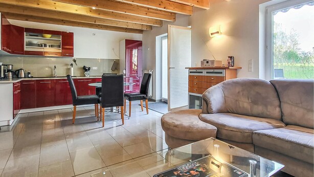 Un soggiorno moderno con un tavolino in vetro, un divano in pelle e un'area pranzo con mobili rossi, con una cucina sullo sfondo.