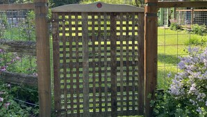 A wooden gate with a lattice design, set in a garden with green grass and flowering plants. - The Loft at Reverie Gardens (Sequim)