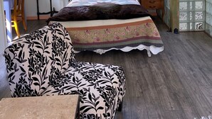 A bedroom with a sloped ceiling, a ceiling fan, a large window, a bed with patterned bedding, a chair, and a wooden desk. - The Loft at Reverie Gardens (Sequim)