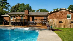 Un jardin avec une piscine, un espace détente avec mobilier de jardin et une maison en briques.