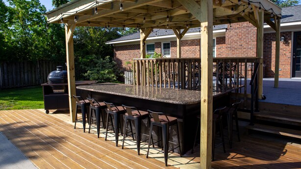 Une terrasse extérieure dotée d’une pergola en bois, d’un coin bar avec des tabourets et d’un barbecue.