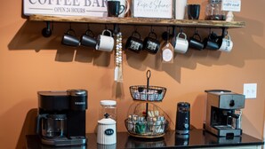 Un comptoir à café avec une enseigne indiquant « Café ouvert 24 heures sur 24 » et une étagère au-dessus, où sont disposées des tasses, ainsi qu’une autre enseigne qui dit « Réveillez-vous et profitez de la journée ».