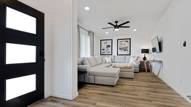 Een moderne woonkamer met een hoekbank, een plafondventilator en kunstwerken aan de muur.