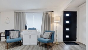 Een moderne woonkamer met twee blauwe fauteuils, een witte kast, een vloerlamp en een zwarte deur met twee ramen.