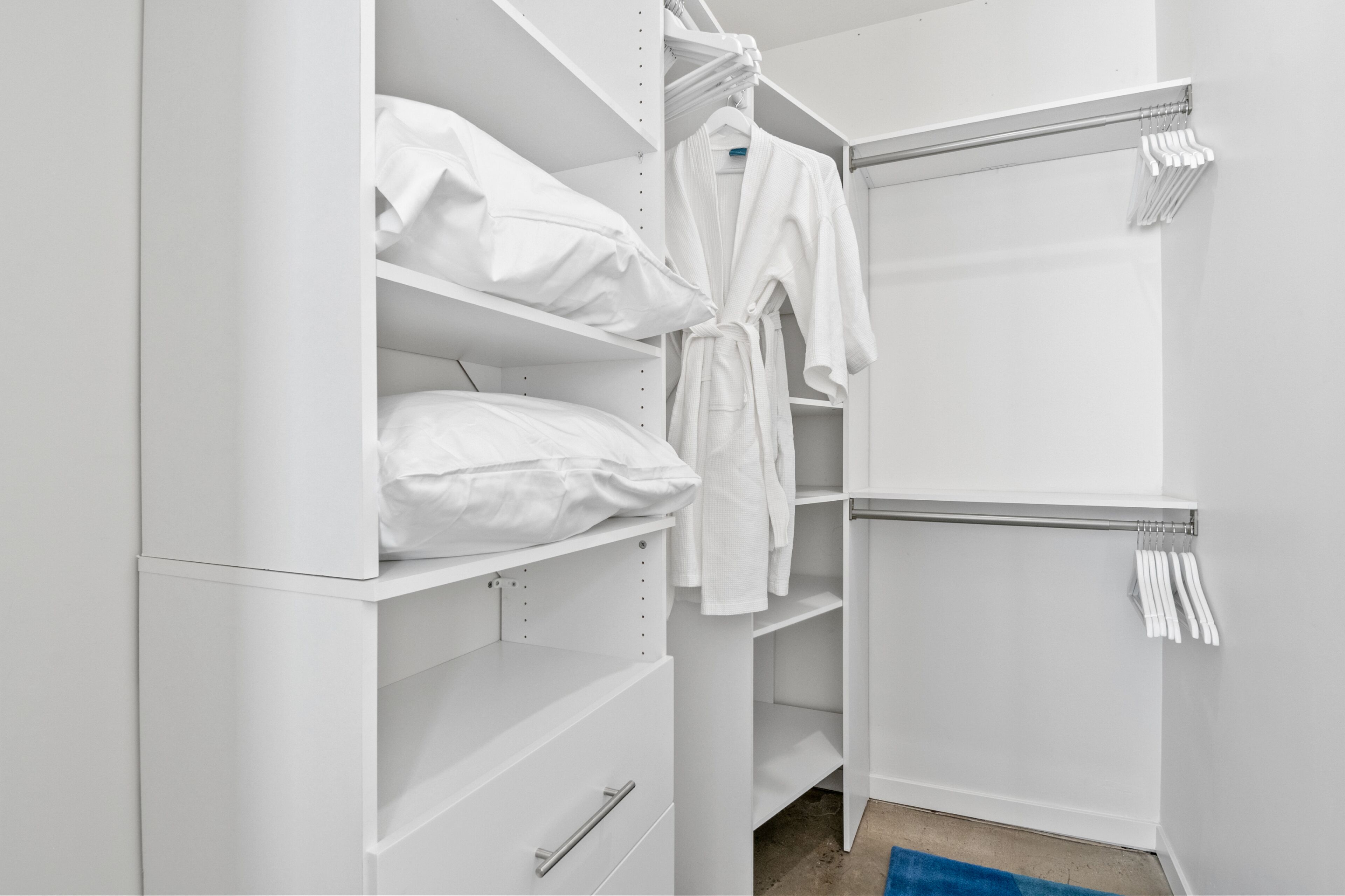 A white walk-in closet with shelves, a robe, and hanging clothes.