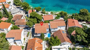 Vista aérea de una zona residencial costera con casas, aguas turquesas cristalinas y un marcador rojo de ubicación.