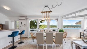Una cocina moderna con comedor, ventanas amplias con vista al mar y una lámpara colgante.