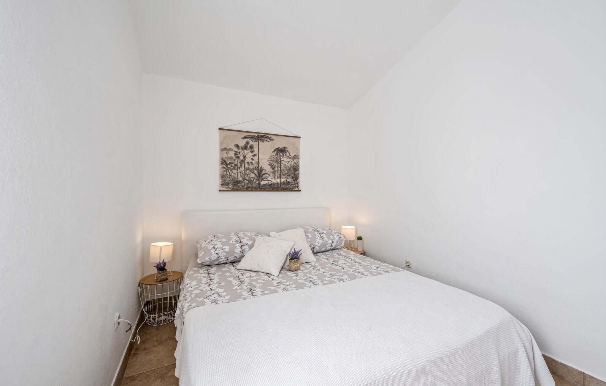Ein Schlafzimmer mit einem Bett, zwei Nachttischen, einem Wandbild und einer kleinen Topfpflanze.