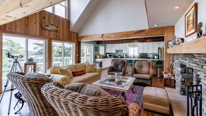 A spacious living area with wicker furniture, a stone fireplace, and a kitchen in the background.