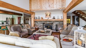A spacious living area with high ceilings, exposed wooden beams, a stone fireplace, and comfortable seating.