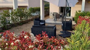 An outdoor patio area with seating, a pergola, and a view of a building with a tiled roof. - Petite Maison Dans Résidence 3 Etoiles Avec Piscine (Belgodère)