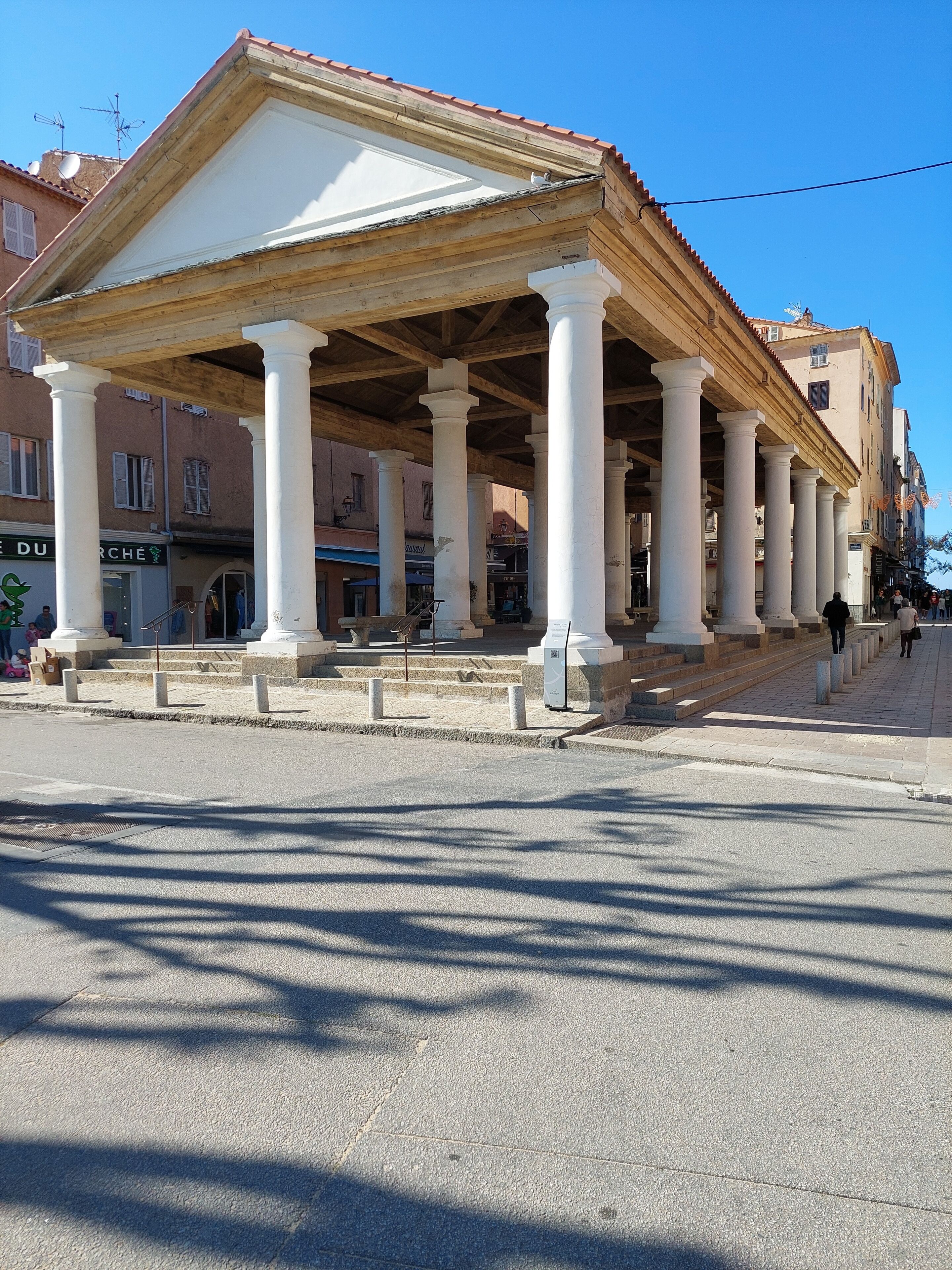A covered outdoor area with white columns, a tiled roof, and a stone floor.