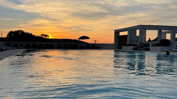 A pool area with lounge chairs and umbrellas, a covered seating area, and a sunset view. - Petite Maison Dans Résidence 3 Etoiles Avec Piscine (Belgodère)
