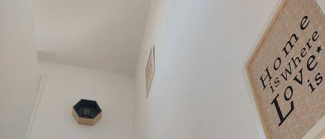 Un escalier avec une rampe en bois menant à un palier. Une plaque décorative accrochée au mur porte l’inscription : « Le foyer, c’est là où se trouve l’amour ».