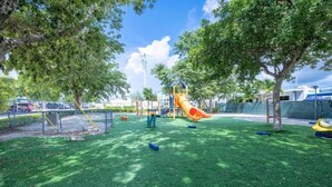 A playground with a slide and swings, surrounded by trees and a fenced area. - Key Largo Relaxing Gataway with Stoning Sunsets Views (Key Largo)