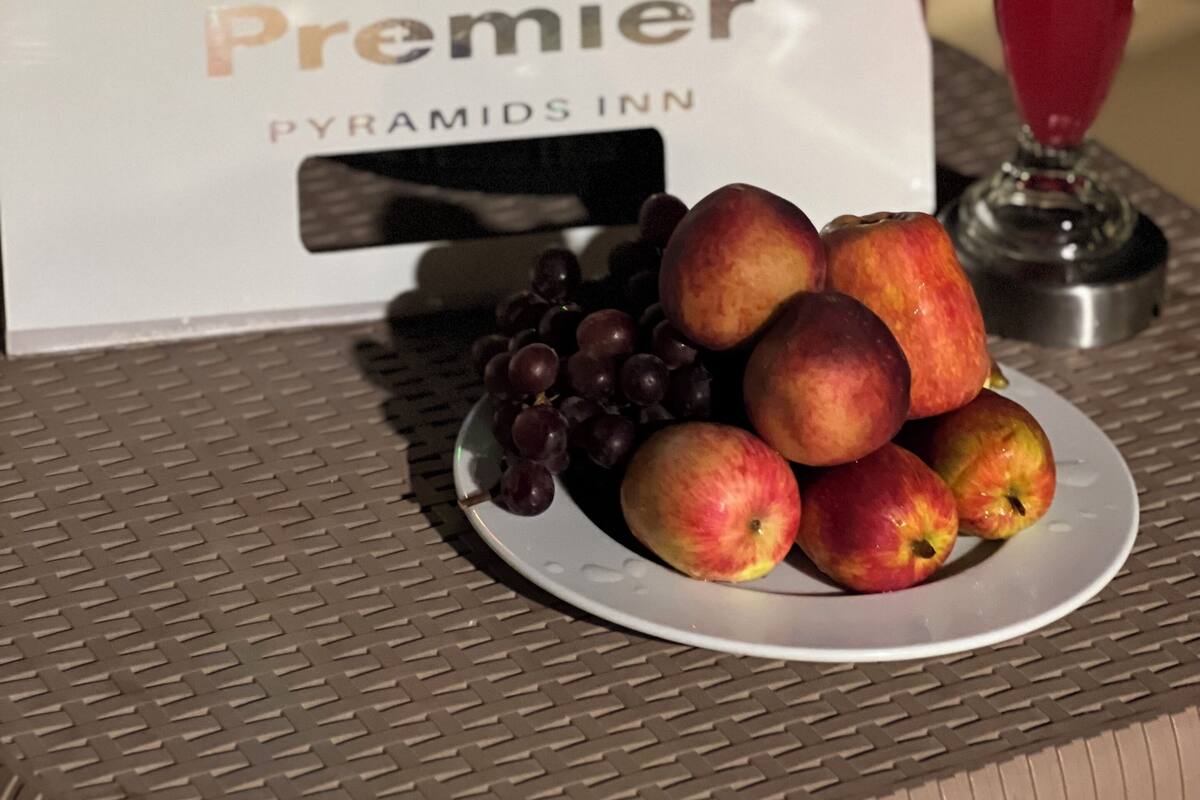 Een bord met fruit, inclusief appels en druiven, op een tafel, een blender en een bord met de tekst Premier Pyramids Inn.